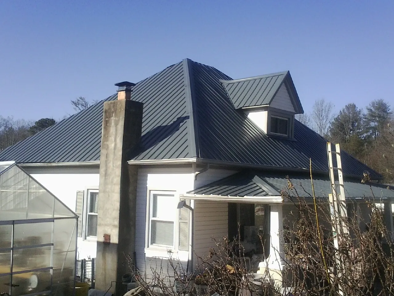 Dark blue standing seam metal roof on a white farmhouse with dormer — Slate & Tile Roof Repair by Roofing Brothers in Old Bethpage