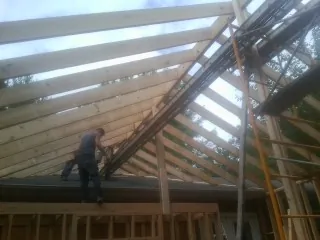 Rafters going up over a new addition with a worker on the wall in Old Bethpage