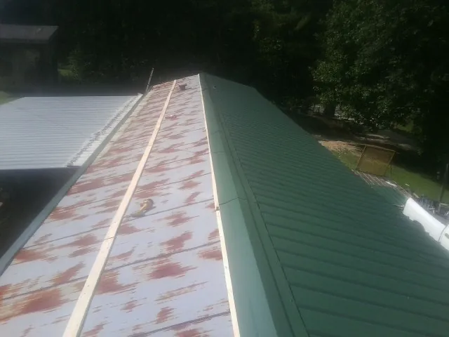 Old rusted panels beside newly installed green metal roofing — Wind Damage Roof Repair by Roofing Brothers in Old Bethpage