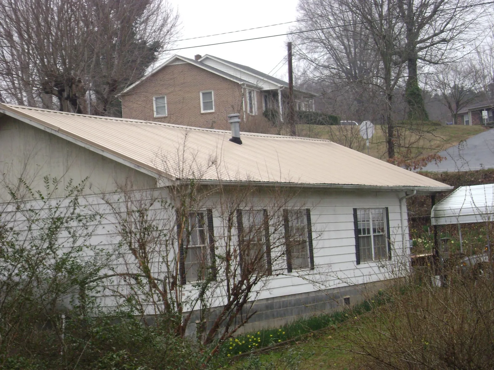 Tan metal roof on a white sided house set into a hillside — Commercial Roofing by Roofing Brothers in Old Bethpage
