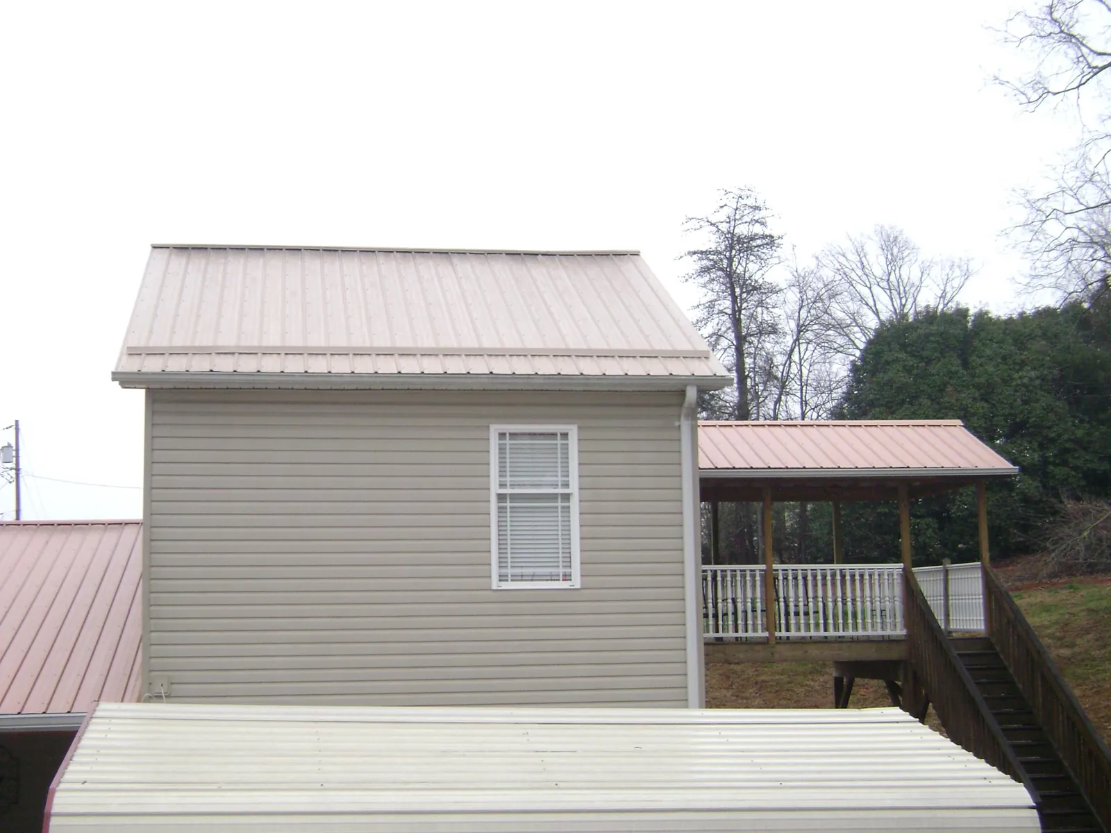 Tan metal roofs on a two story addition and attached porch, from a Roof Replacement job in Old Bethpage