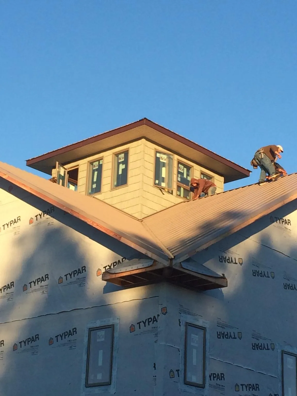 Roofers working around a rooftop cupola on a new metal roof at sunset — Roof Waterproofing in Old Bethpage by Roofing Brothers